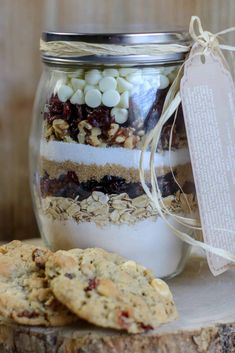 cookies and marshmallows in a glass jar on top of a tree stump