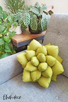 a green pillow sitting on top of a gray couch next to potted plants and a wooden table