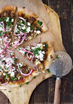 a pizza with onions, cheese and herbs on a cutting board next to a spatula