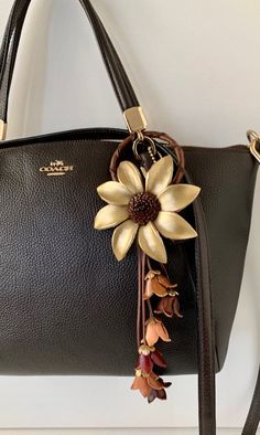 a black handbag with a flower on the front and side hanging from it's strap