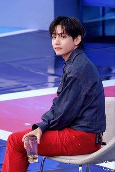 a young man sitting on top of a chair holding a drink in his hand and looking off to the side