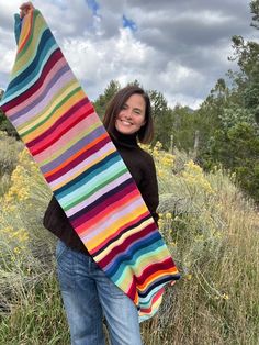 a woman holding up a multicolored striped blanket