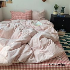 an unmade bed with pink sheets and checkered bedspread in a bedroom