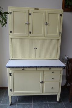 an old fashioned kitchen cabinet with marble top and drawers on the bottom, next to a wooden chair