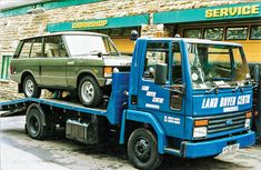 a flatbed tow truck with a green car on it's back in front of a service store