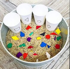 four cups with numbers on them are in a bucket filled with oats and colored shapes