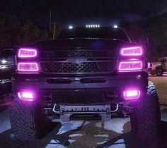 the front end of a black truck with purple lights on it's headlamps