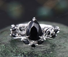 a black diamond ring sitting on top of a green stone covered rock with leaves and vines around it