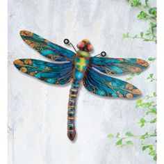 a blue and yellow dragonfly sitting on top of a white wall next to green plants