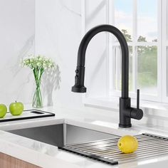 a kitchen sink with a black faucet and some green apples on the counter