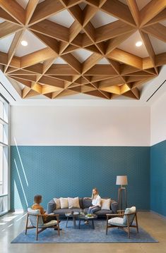 two people sitting on a couch in a room with blue walls and wooden ceilinging