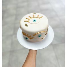 a hand holding a white cake with gold decorations on it's face and eyes