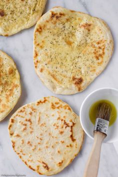 three flat breads on a marble surface with a brush and bowl next to them