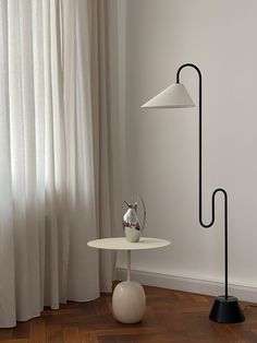 a white table with a lamp on it next to a curtained window in a room