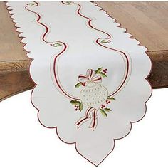 a white table runner with holly and bells on it, sitting on top of a wooden bench