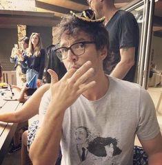 a man with glasses and a crown on his head sitting at a table in front of other people