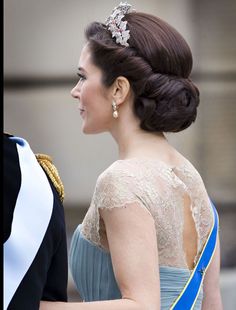 a woman in a blue dress and tiara walking next to a man in a black suit