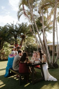 a group of people sitting at a picnic table with drinks in front of palm trees