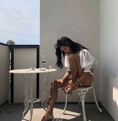 a woman sitting on a chair next to a table with a glass of wine in it