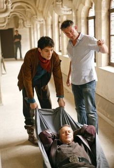 two men standing over a man laying on the ground in a room with large windows