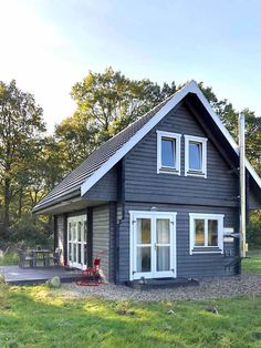 a small gray house sitting on top of a lush green field next to a forest