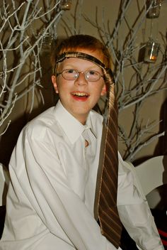 a young man wearing glasses and a neck tie smiling at the camera with bare branches in the background