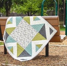 a park bench with a quilted blanket on it's back in front of a playground