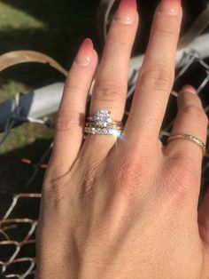 a woman's hand with two rings on it and a chain link fence in the background