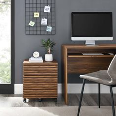 a computer desk with a monitor and keyboard on it in front of a gray wall