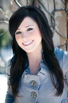 a woman with long black hair is posing for a photo in front of a tree