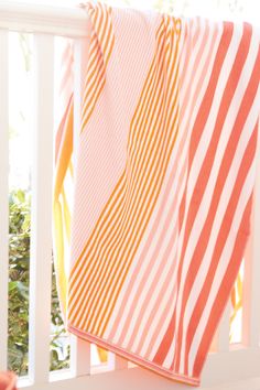 an orange and white striped towel hanging on a rail in front of a porch window