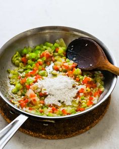 a pan filled with vegetables and seasoning next to a wooden spoon