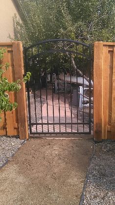 an iron gate is open on the side of a driveway with gravel and trees in the background