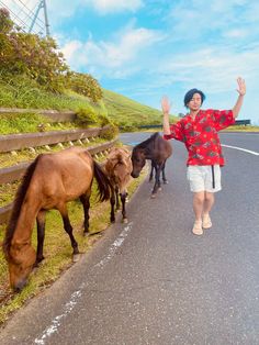 a woman standing next to two horses on the side of a road with her arms in the air