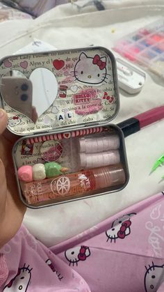 a hello kitty tin with various items in it on a bed next to a mirror