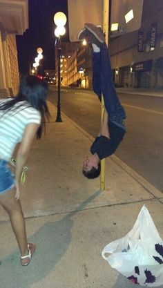 two people doing tricks on the sidewalk at night with one upside down in the air