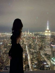 a woman standing on top of a tall building looking out at the city lights and skyscrapers