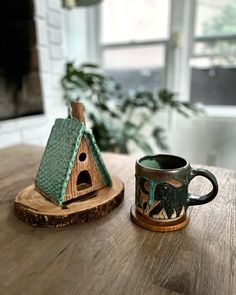 a coffee cup sitting on top of a wooden table next to a small house shaped like a birdhouse