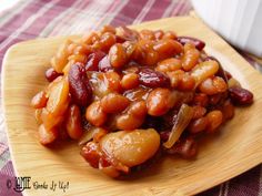 a wooden plate topped with beans and meat on top of a checkered table cloth