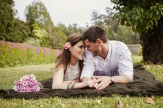 a man and woman laying on a blanket in the grass with their hands around each other