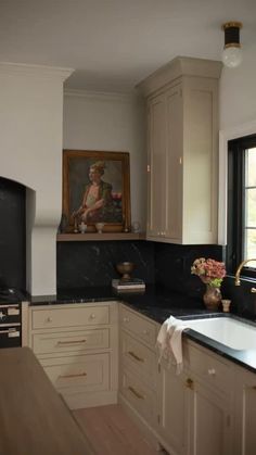 a kitchen with white cabinets and black counter tops, an oven and sink in front of a window