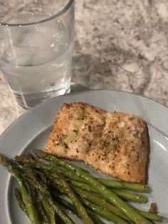 a piece of salmon and asparagus on a plate next to a glass of water