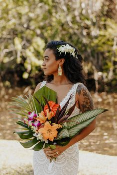 a woman in a white dress holding a bouquet of flowers and greenery on her wedding day