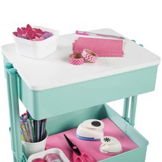 a small table with some craft supplies on it and a bowl of pink flowers in the background