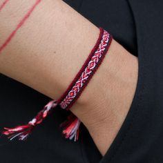 a woman wearing a red and white bracelet with tassels on her arm,