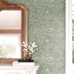 a mirror and vase with flowers in front of a wallpapered room that looks like it has been painted