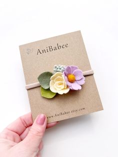 a hand is holding an adorable flower headband on a card with the words antibabee