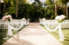 rows of chairs with white sashes and flowers on them at an outdoor wedding ceremony