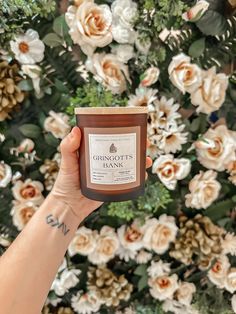 a hand holding up a jar of candle in front of a floral wall with roses