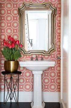 a white pedestal sink sitting under a mirror next to a vase with flowers in it